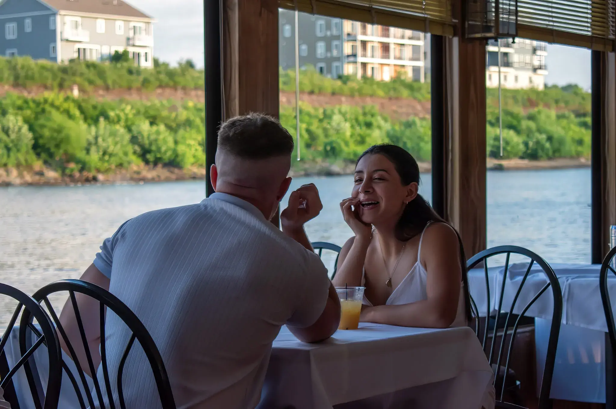 A couple dining at a white-linen window table as the Ohio River passes outside