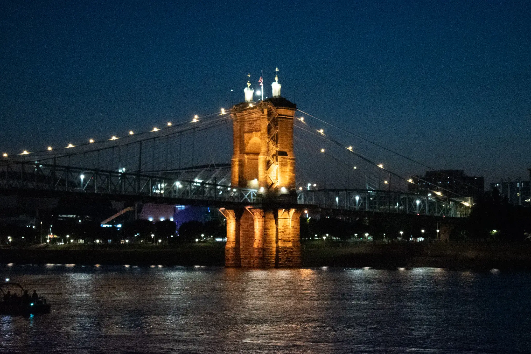 The Roebling Suspension Bridge lit at night, seen from the deck of a riverboat on the Ohio River